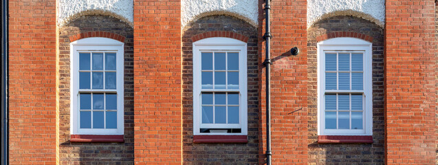 Obraz premium Red Brick Facade with Three Tall White Windows in Symmetrical Architecture