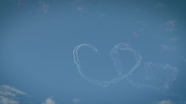 Two planes completing a loop maneuver with smoke trails in a cloudy blue sky.