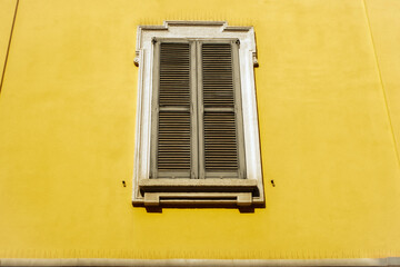 Fototapeta premium Vintage window with wooden shutters on a bright yellow building facade. Minimal architecture and geometric composition create a concept of Mediterranean design, travel, and urban culture.