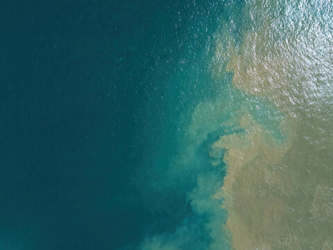 Aerial view of sediment plumes mixing with deep blue ocean water, showing contrast between murky and clear sea currents in Jinotepe, Carazo, Nicaragua.