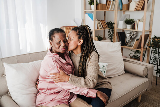 Daughter kissing mother sitting on sofa at home