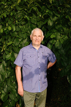 Confident mature man stands smiling outdoors by green leaves