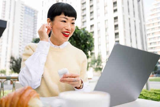 Freelance worker on video call with laptop at outdoor cafe having breakfast