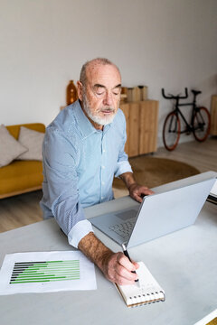 Businessman with laptop writing in notepad sitting at desk