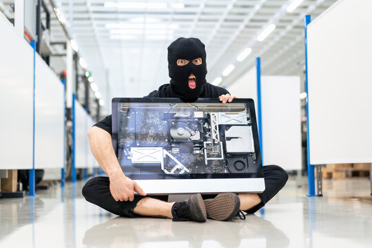Surprised thief with computer sitting on floor at industry