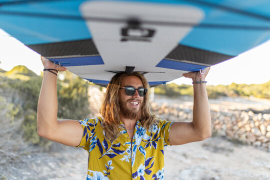 Man carrying paddleboard on head at beach during sunset