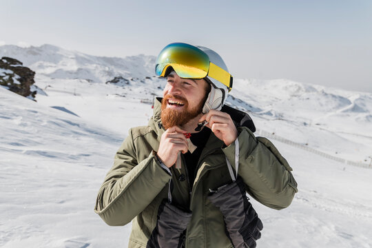 Smiling young man with beard fastening skiing helmet