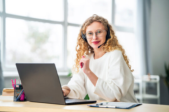 Smiling saleswoman wearing headset near laptop in office