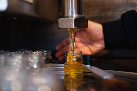 A woman monitors the machine filling a glass jar with golden honey