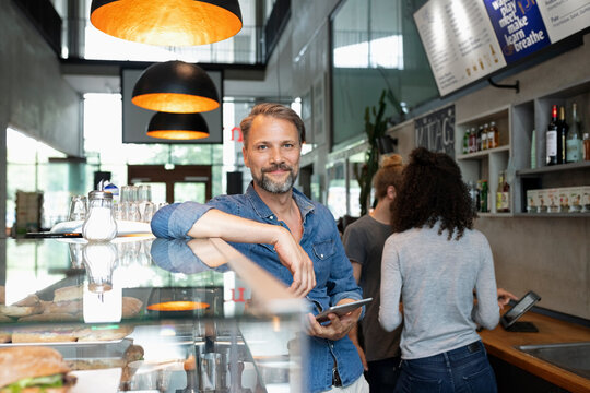 Smiling cafe owner standing with tablet PC in cafe