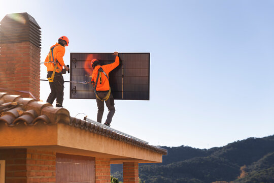 Technicians installing solar panel on roof in Barcelona with safety gear