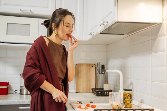 Woman eating tomato while cooking at home on New Years Eve