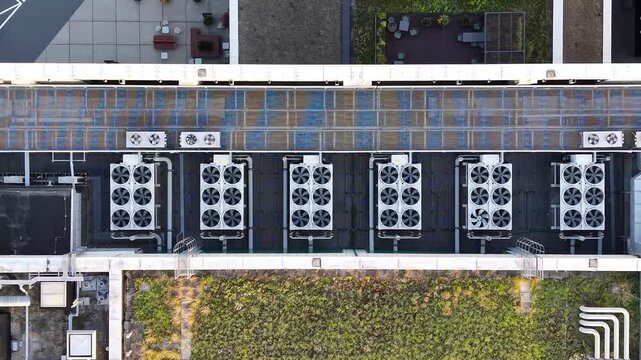 Air conditioning units on rooftop of modern office building, showcasing multiple cooling systems with visible fans and pipes, surrounded by green landscaping and urban architecture