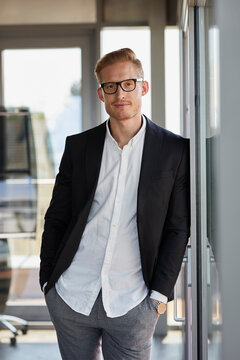 Portrait of confident businessman in office leaning against window