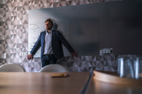 Businessman standiing in boardroom with back to a magnet wall, framed by arrows