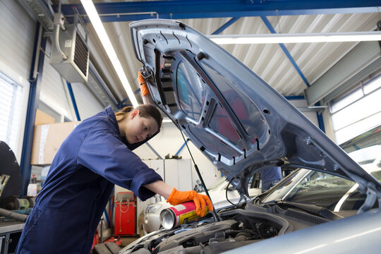 Young woman working in repair garage, checking engine