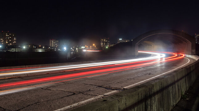 Nighttime long exposure of vibrant vehicle light trails flowing along a highway past an arched underpass.