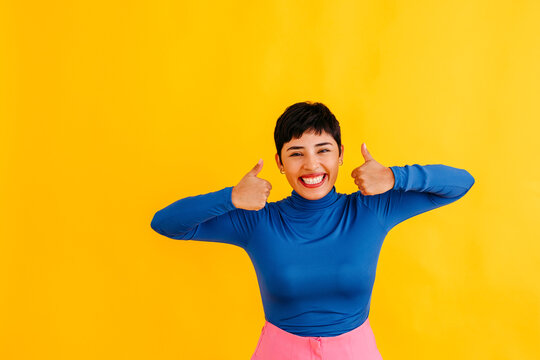 Happy young woman showing thumbs up against yellow background