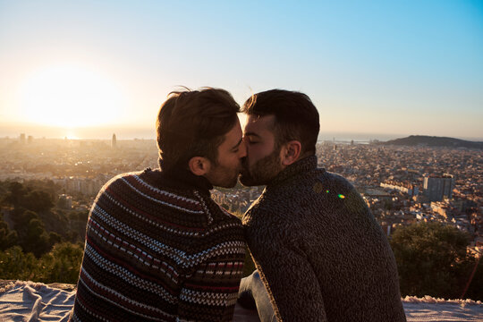 Gay boyfriends kissing while sitting on observation point, Bunkers del Carmel, Barcelona, Spain