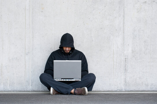 Hacker with laptop sitting in front of concrete wall