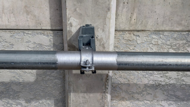 Steel pipe secured with a metal clamp bracket and mounted onto a concrete wall support pillar at an industrial building construction site