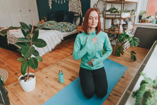 Woman with eyes closed meditating on exercise mat at home