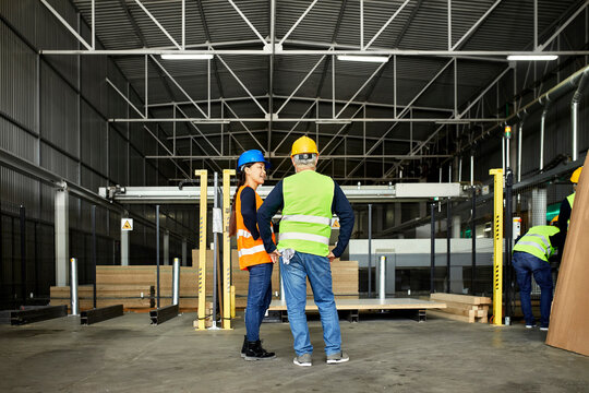 Rear view of male and female worker standing in factory workshop