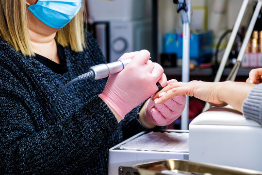 Manicurist working on client nails using nail drill in beauty salon