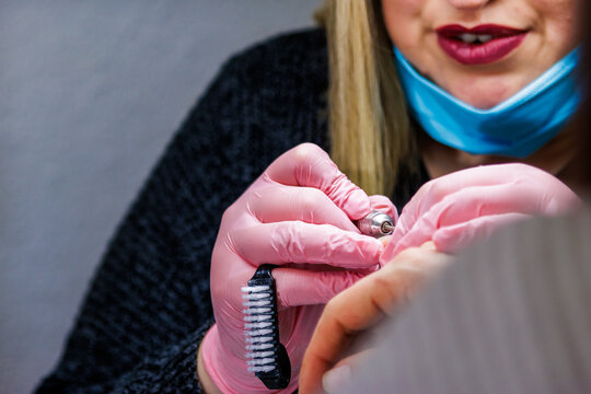 Professional manicurist at beauty salon providing nail care using electric file and gloves