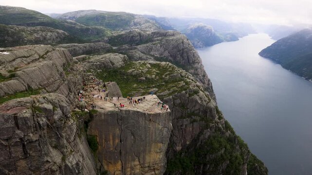 Many hikers walking on Preikestolen above a large fjord in Norway
