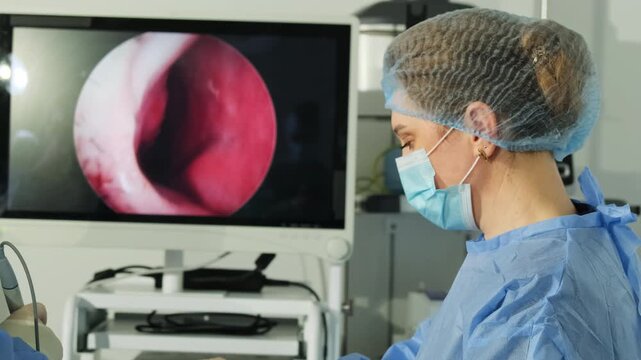 Plastic surgeon guides thin endoscope into nasal passage. Woman assistant attentively helps during delicate operation. Slow motion