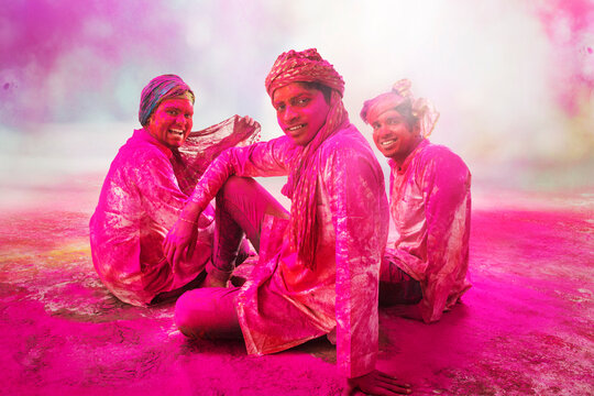 Young Indian Men sitting on floor,covered in colored powder during holi color festival