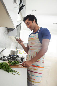 Young man chopping vegetables and using a mobile phone