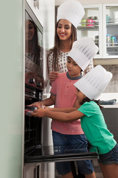 Mother with daughter and son wearing chefs hat and baking cake in kitchen