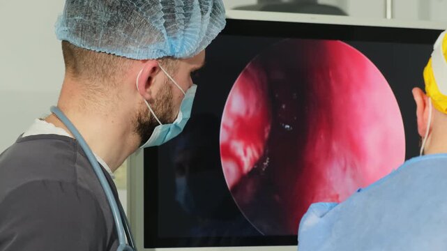 High-tech operating room screen shows internal surgical examination footage. Doctors watch nasal endoscopy duration in surgery room
