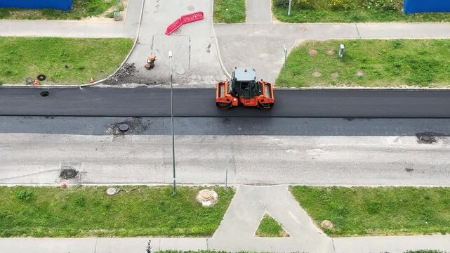 Road roller operates on a highway while nearby traffic continues, infrastructure maintenance, transport engineering, industrial roadwork, aerial drone perspective.