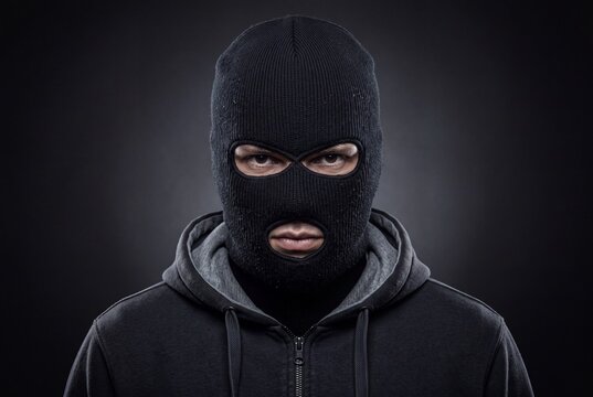 Portrait of a man wearing a black balaclava ski mask and a hooded sweatshirt against a dark background