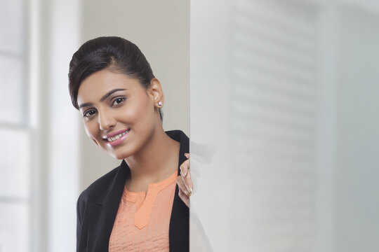 Smiling Businesswoman behind glass pane looking at camera