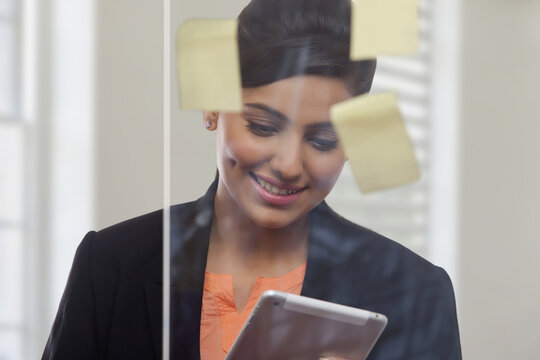 Businesswoman behind glass pane with adhesive notes using digital tablet in office 