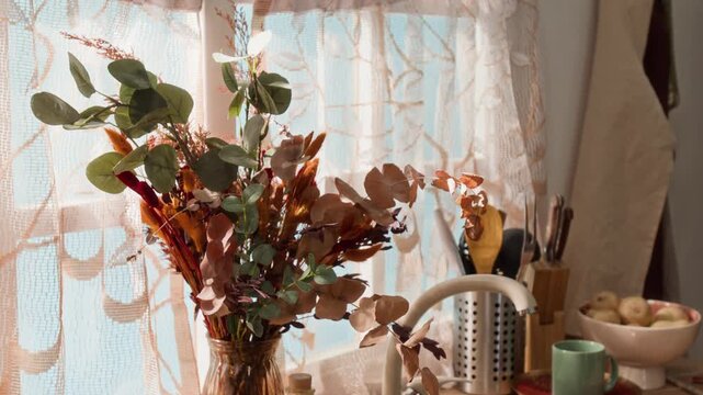 Dried eucalyptus bouquet in vase standing on counter near window. Footage is suitable for home decor advertising, kitchenware marketing, or lifestyle brand promotions