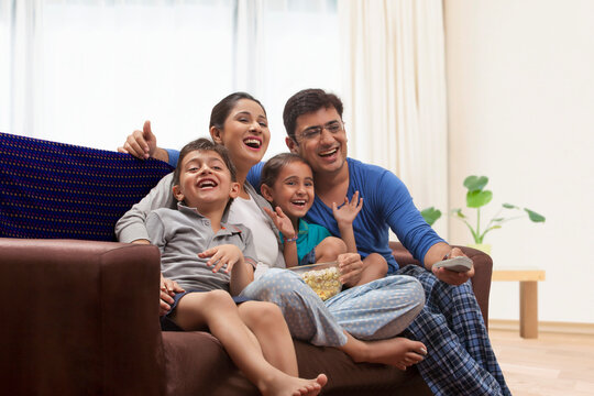 Family in pyjamas watching TV and eating popcorn