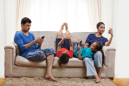 Family using cell phones and digital tablets in living room