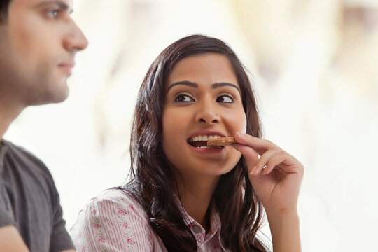 Woman biting a biscuit half smiling looking at her husband