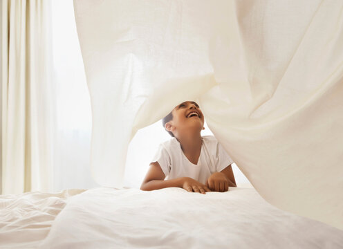 Young boy playing under white bed sheet in bedroom