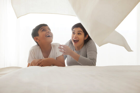 Mother and son playing under white bed sheet in bedroom