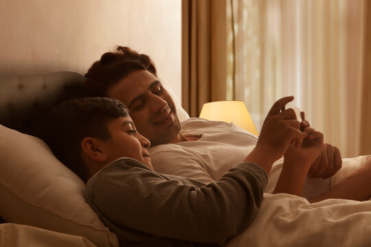 Father and son using smart phone on bed