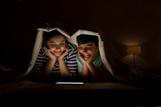 Mother and son watching digital tablet together lying in bed under the blanket