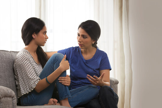 Mother and teenage daughter conversing in living room