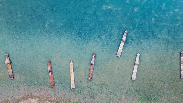Bamboo rafts floating in shallow turquoise river water beside a pebbly shoreline, captured from above in Guilin, China, for travel and tourism concepts.