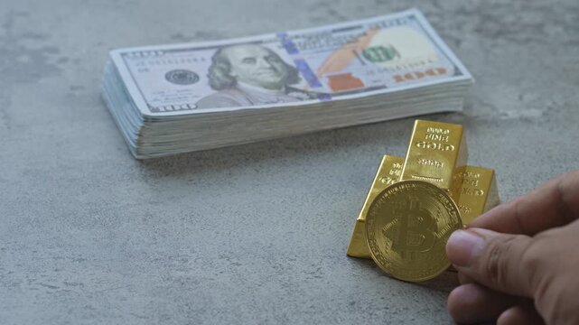 Hand places gold bitcoin coin of gold bars and stack of US dollar bills for modern wealth assets concept